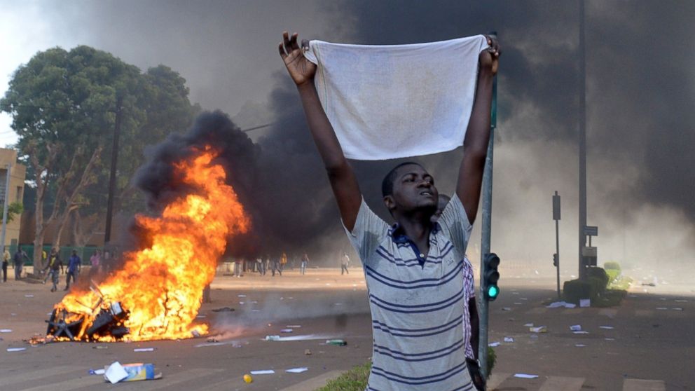 A protester holds a white cloth as cars and documents burn outside the parliament in Ouagadougou, Burkina Faso, Oct. 30, 2014. 