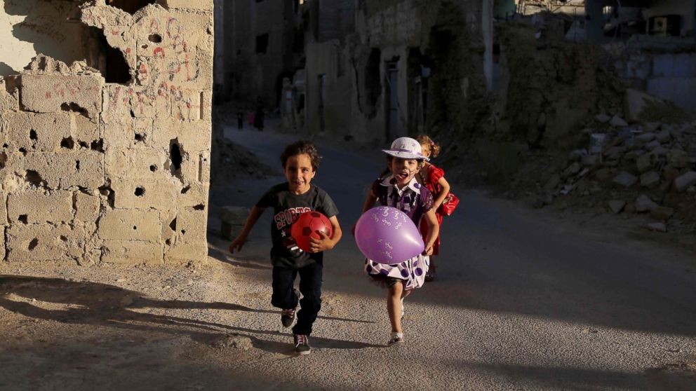 Syrian children run amidst heavily damaged buildings during an activity organized by a charity group in Jobar, a rebel-held district on the eastern outskirts of the capital Damascus, ahead of Eid al-Fitr holyday in the war-torn country on July 5, 2016. 