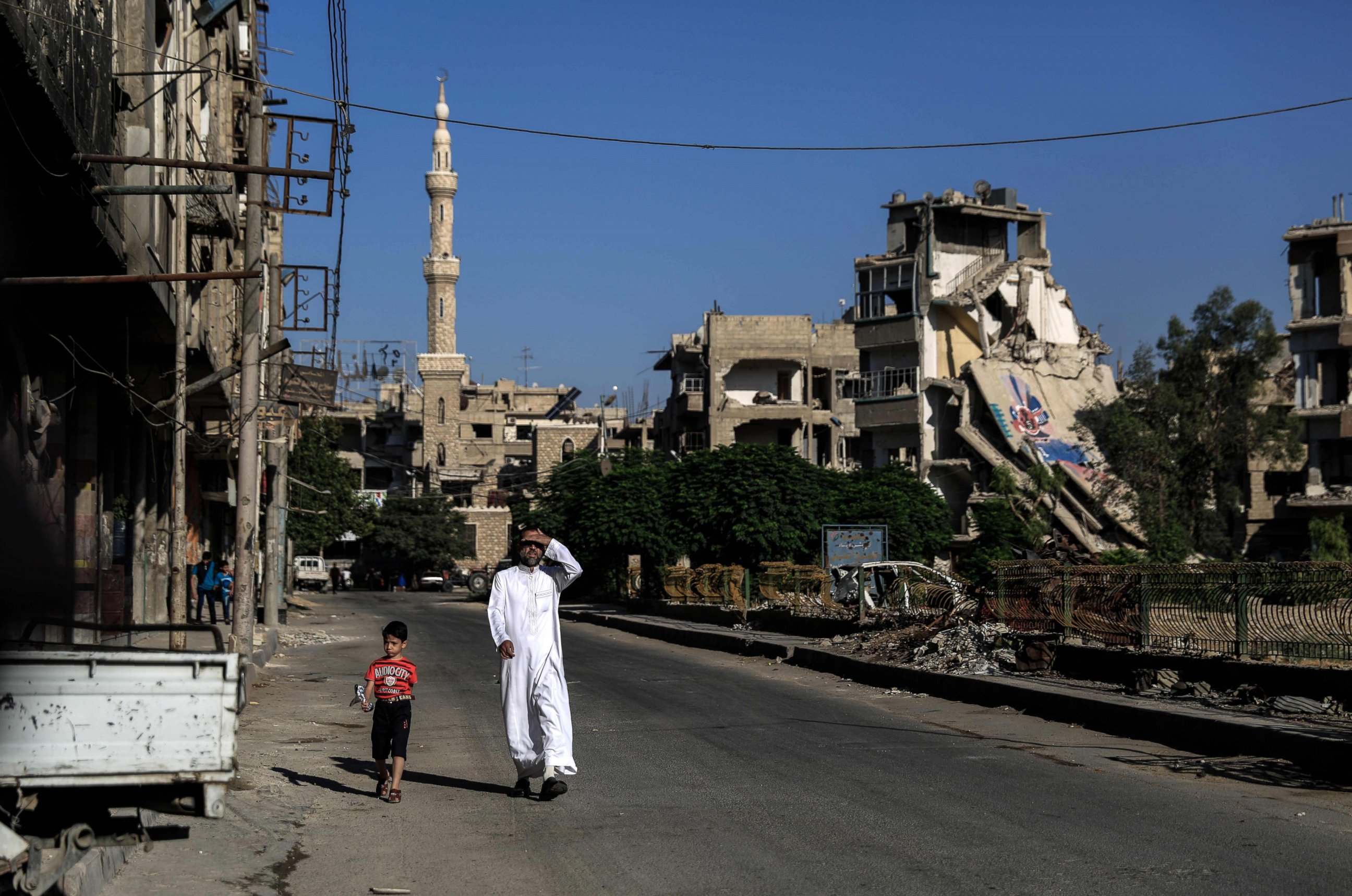 PHOTO: A Syrian man walks with his son along a destroyed street in the rebel-held town of Douma, east of the capital Damascus, on the first day of Eid al-Fitr, which marks the end of the Muslim fasting month of Ramadan on July 6, 2016.