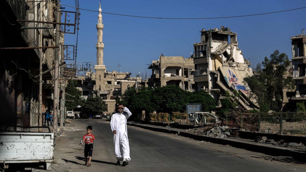 PHOTO: A Syrian man walks with his son along a destroyed street in the rebel-held town of Douma, east of the capital Damascus, on the first day of Eid al-Fitr, which marks the end of the Muslim fasting month of Ramadan on July 6, 2016.