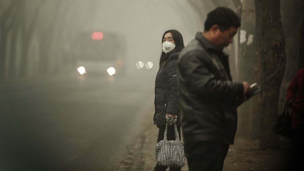 A woman wears a face mask next to traffic shrouded in heavy smog on Dec. 1, 2015 in Beijing, China.