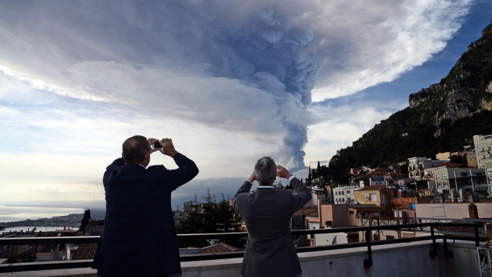 PHOTO: People take pictures of the smoke rising over the city of Taormina during an eruption of the Mount Etna, one of the most active volcanoes in the world, near Catania, Dec. 4, 2015. 