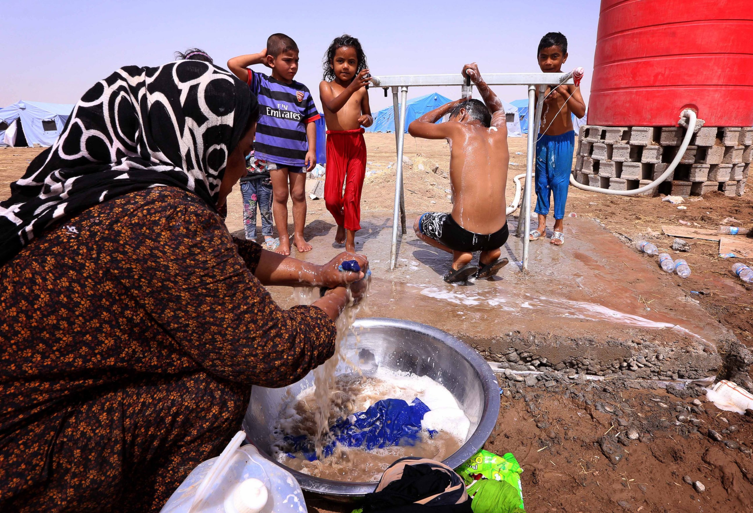 PHOTO: A displaced Iraqi woman washes her family's laundry as children shower outside their tent at a temporary camp set up to shelter civilians fleeing violence in Iraq's northern Nineveh province on June 13, 2014.