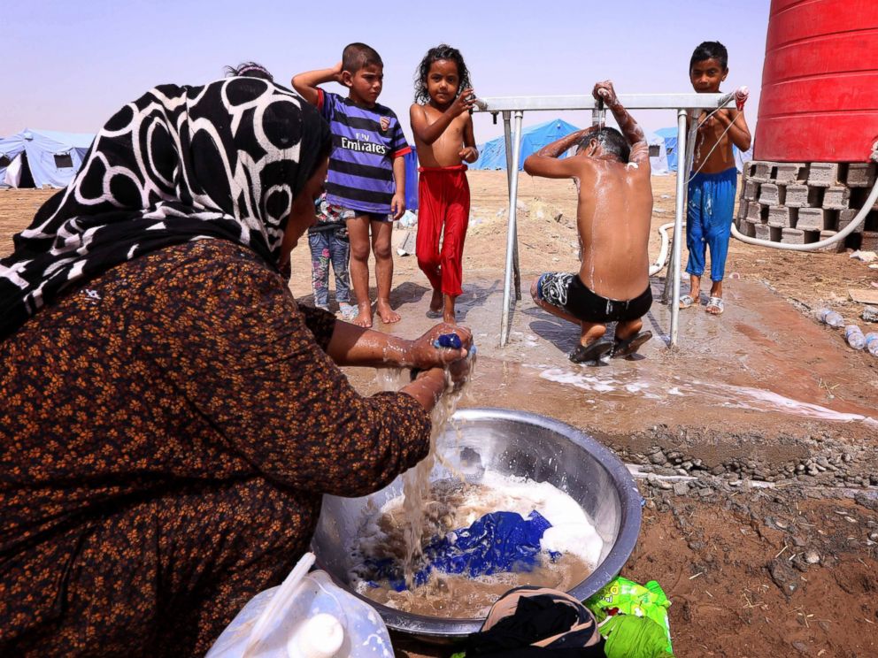 PHOTO: A displaced Iraqi woman washes her familys laundry as children shower outside their tent at a temporary camp set up to shelter civilians fleeing violence in Iraqs northern Nineveh province on June 13, 2014.