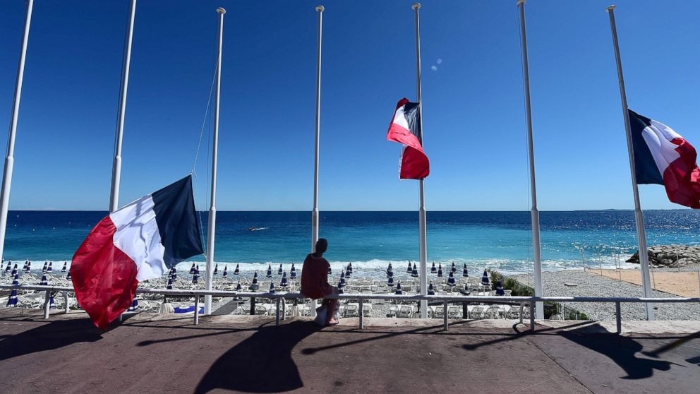 A woman sits under French flags lowered at half-mast in Nice on July 15, 2016, following the deadly Bastille Day attacks. 