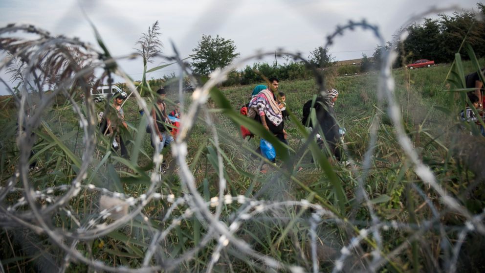 Refugees walk along a barbed wire barrier a the border of Hungary and Serbia, near Roszke, Hungary, Sept. 14, 2015.