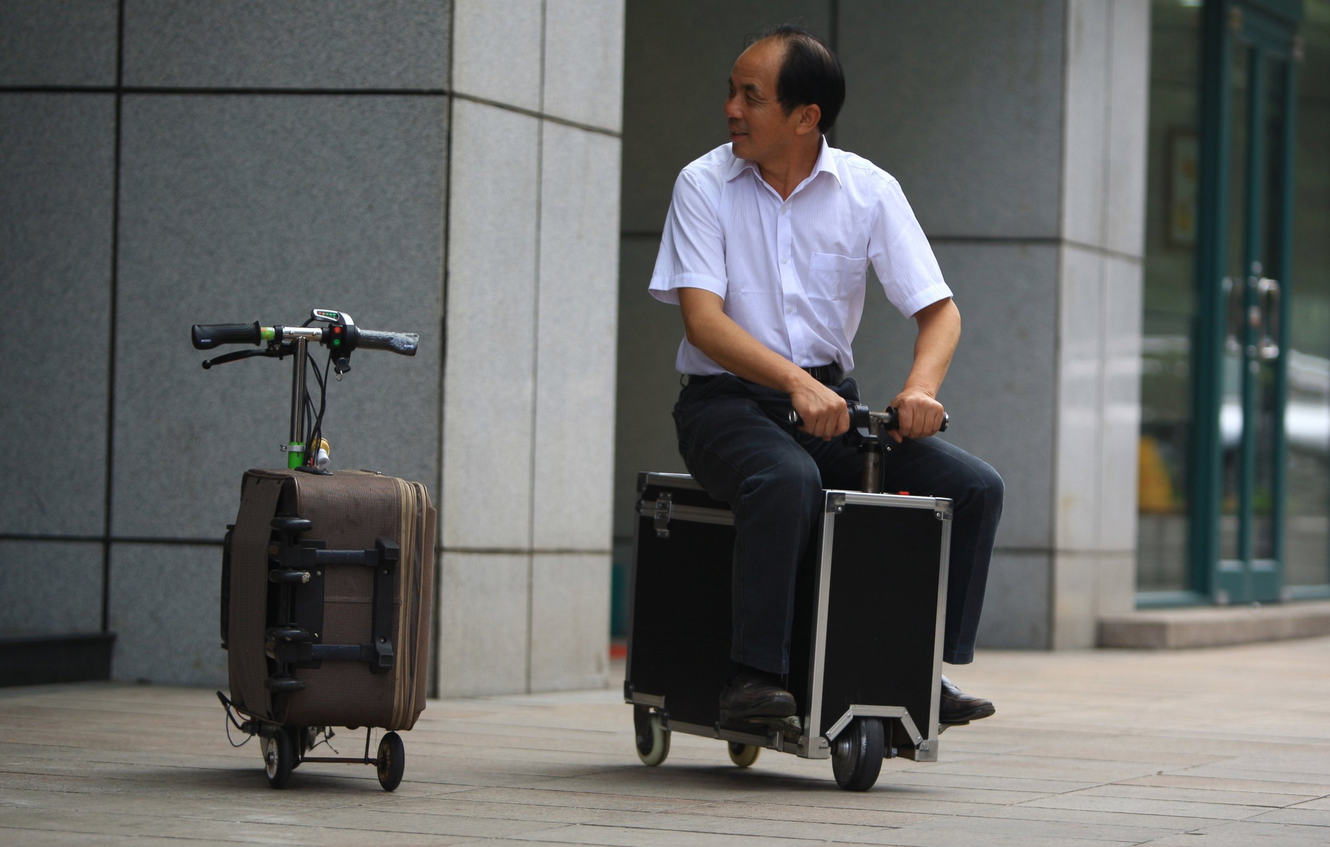 PHOTO: Chinese farmer He Liangcai rides a motorized scooter suitcase that he invented on the street in Changsha, central China's Hunan province, May 28, 2014. 