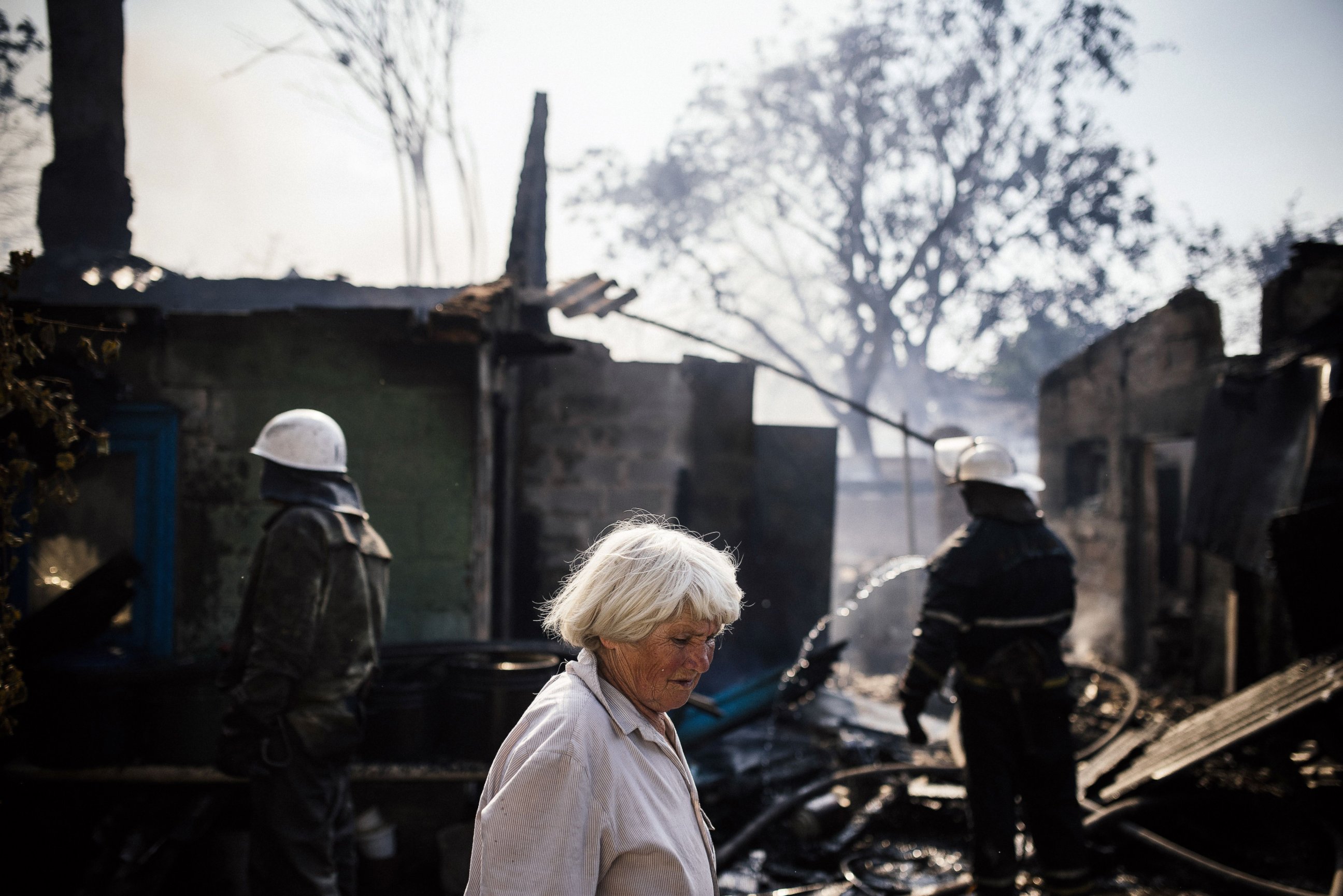 PHOTO: A woman walks past firemen and burnt houses after shelling in Donetsk, Aug. 16, 2014.