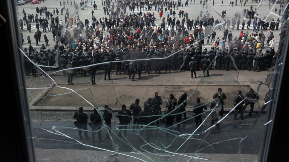 A photo taken through a shattered window shows pro-Russian protesters gathered in front of Ukrainian police officers, who are standing guard of the Kharkiv regional state administration building on April 8, 2014. Ukrainian policemen were injured as a result of an operation to free the administration building from pro-Russian separatists.