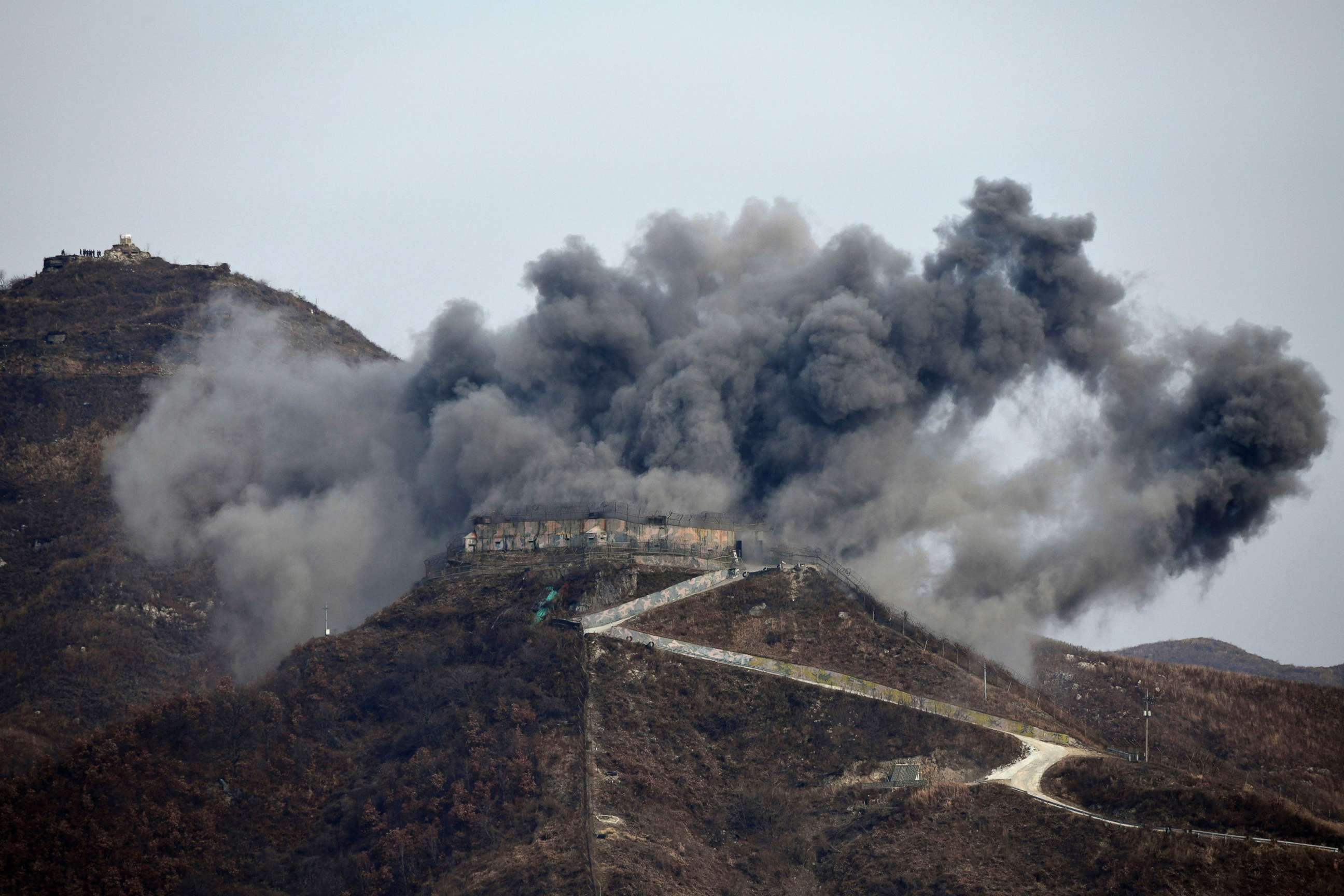 PHOTO: Smoke and debris from an explosion rises as part of the dismantling of a South Korean guard post, Nov. 15, 2018, in the Demilitarized Zone dividing the two Koreas in Cheorwon, as a North Korean guard post sits high in the upper left.