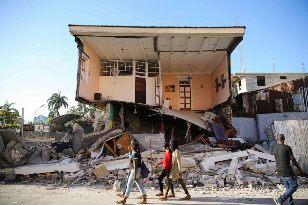 PHOTO: People walk past a home destroyed by the earthquake in Les Cayes, Haiti, Saturday, Aug. 14, 2021.