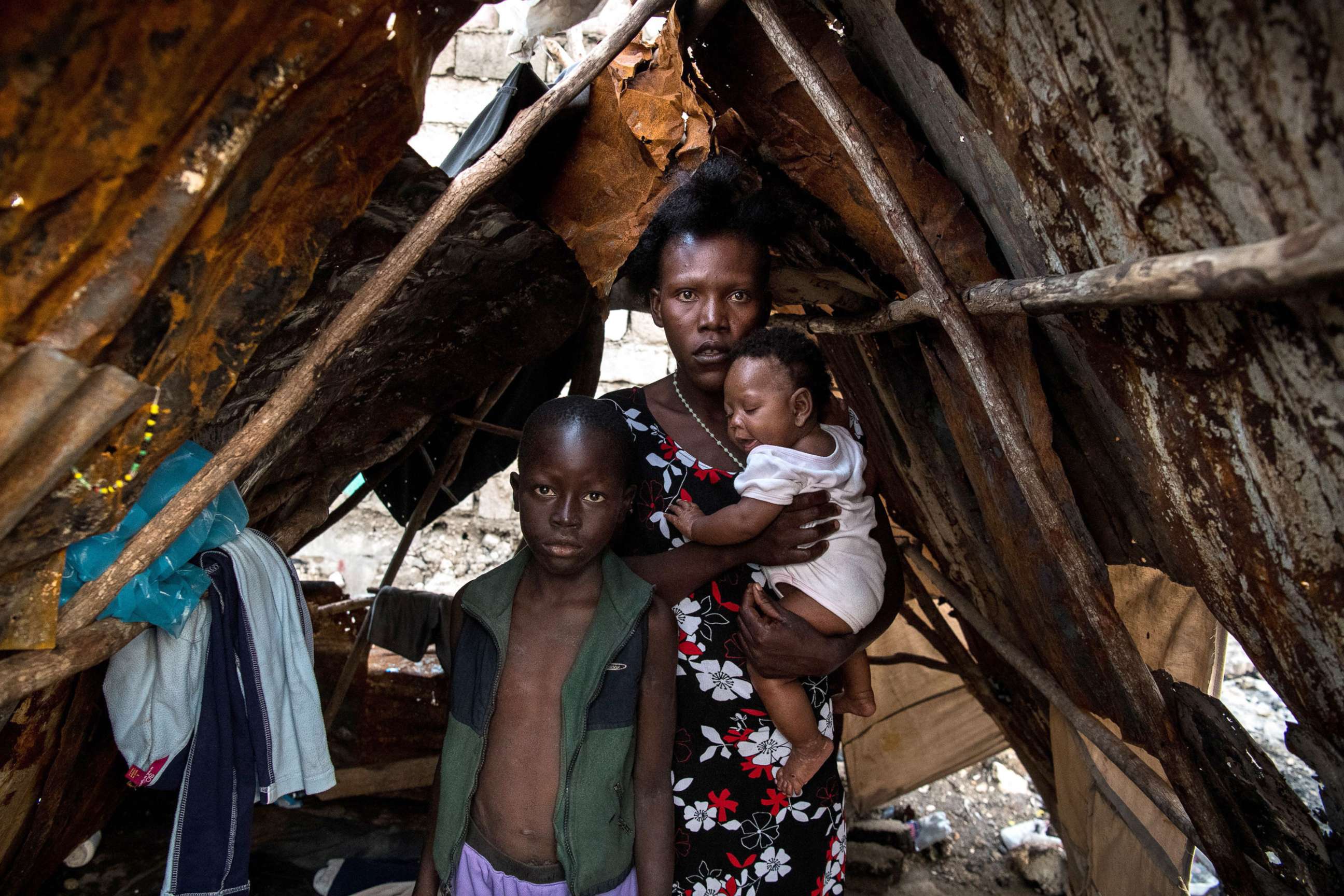 PHOTO: A family stands inside a makeshift shelter built on the site of their home which was burned during gang war activity, on May 25, 2019 in Port-au-Prince, Haiti. 