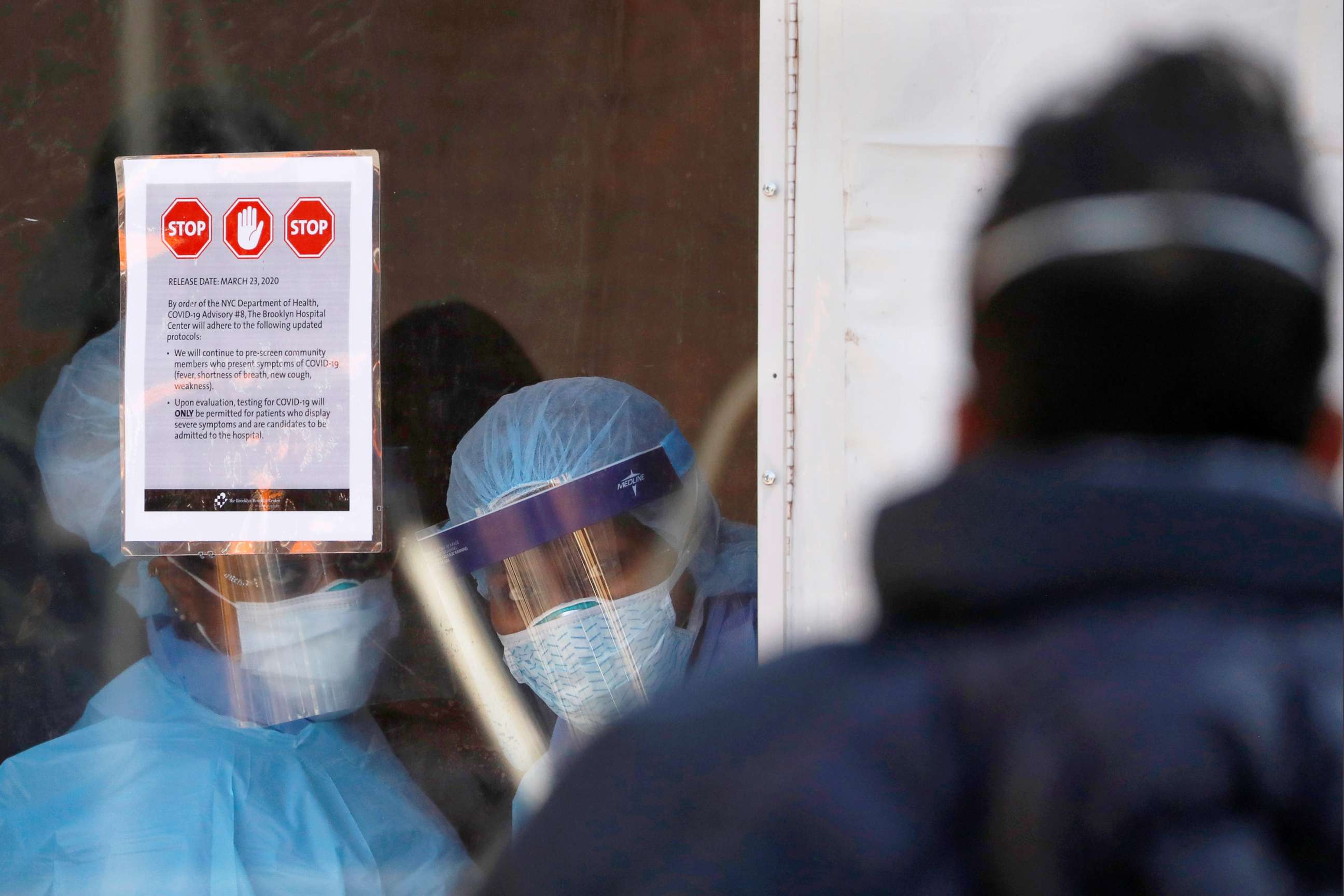 PHOTO: Health workers in protective gear peer at people lining up to enter a tent which was constructed to test people for the coronavirus disease (COVID-19) outside the Brooklyn Hospital Center in Brooklyn, New York City, March 27, 2020.
