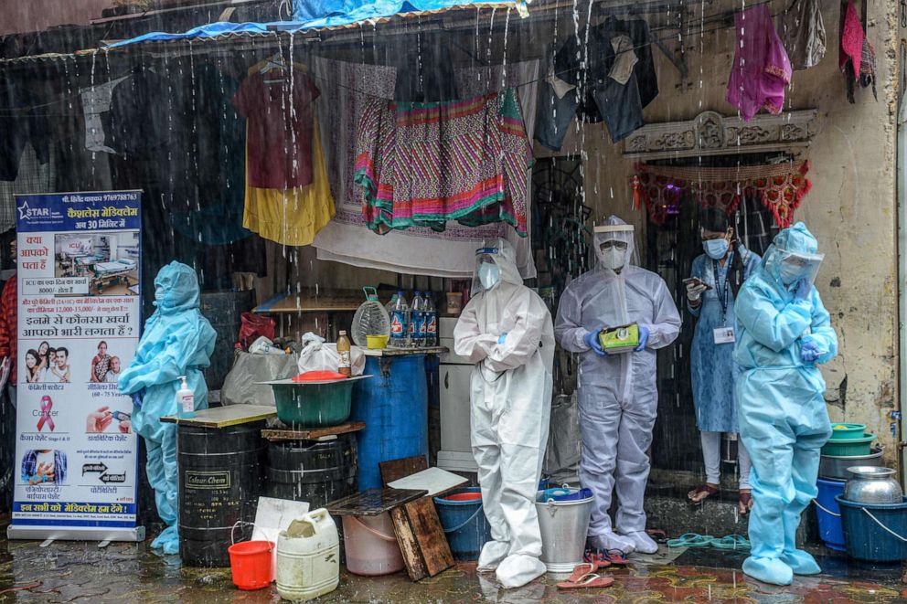 PHOTO: Health workers wearing personal protective equipment suits take shelter amid heavy rain while conducting a COVID-19 screening in Mumbai, India, on Aug. 12, 2020.