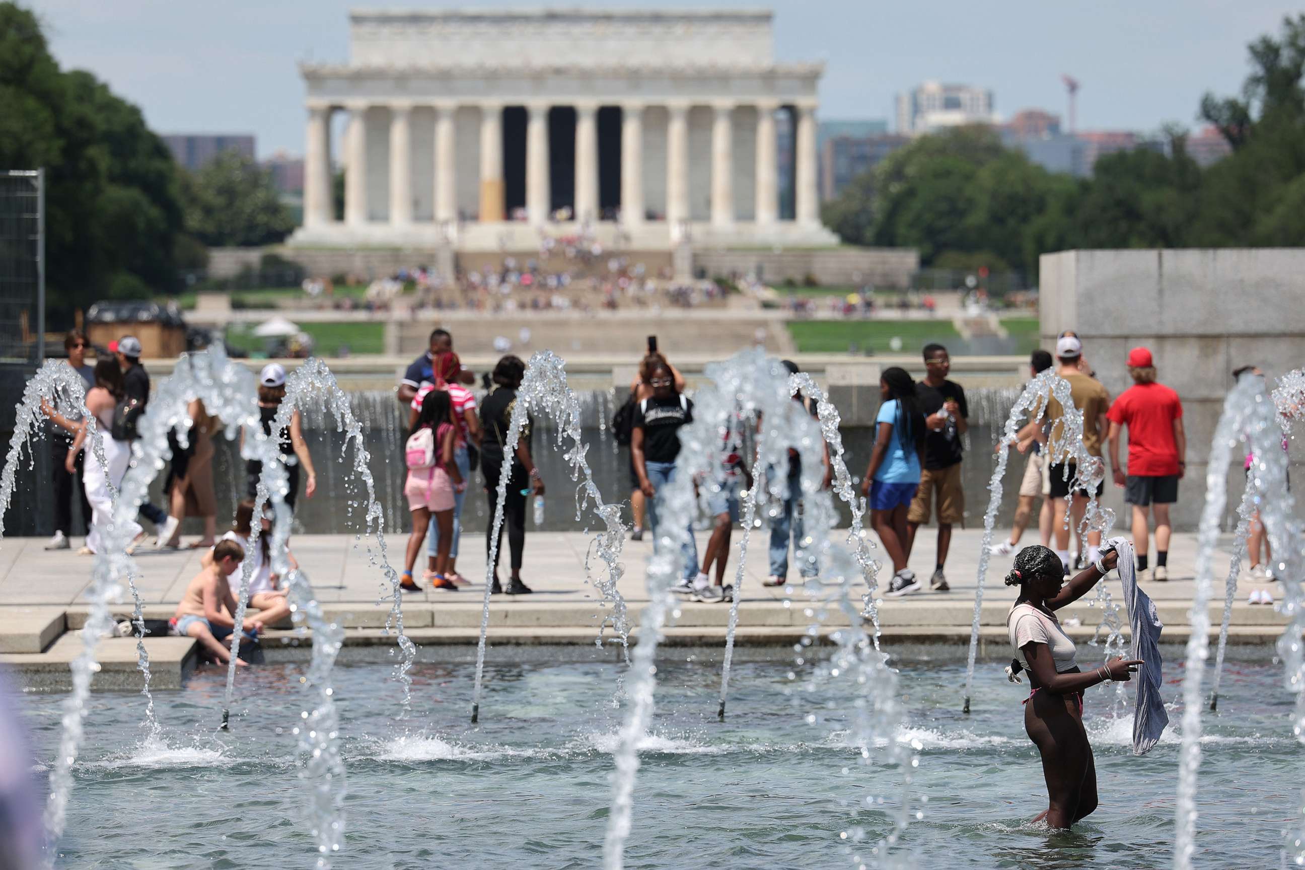 PHOTO: Visitors and tourists to the World War II Memorial seek relief from the hot weather in the memorial's fountain, July 3, 2023, in Washington, D.C.