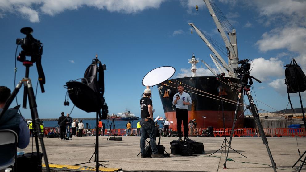 PHOTO: Journalists work with the Dutch flagged hantavirus-stricken cruise ship MV Hondius in the background in the port of Granadilla de Abona on the island of Tenerife in Spain's Canary Islands on May 11, 2026.