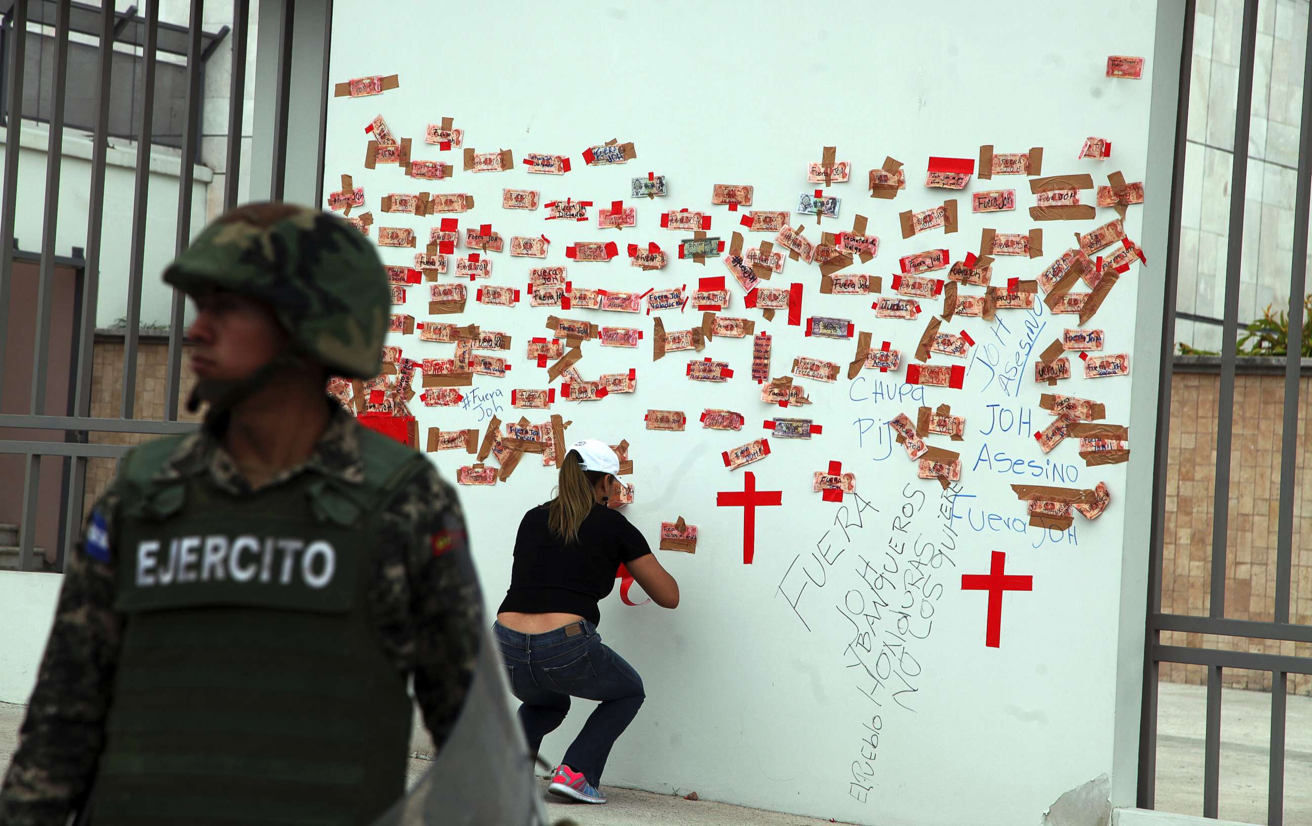 PHOTO: A protester tapes Honduran money inscribed with political slogans alongside crosses representing people killed in post-election violence, on the outside of the central bank in Tegucigalpa, Honduras, Jan. 7, 2018.