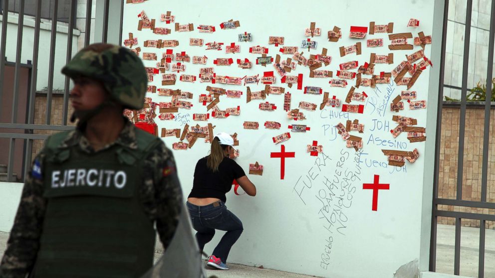 A protester tapes Honduran money inscribed with political slogans alongside crosses representing people killed in post-election violence, on the outside of the central bank in Tegucigalpa, Honduras, Jan. 7, 2018.