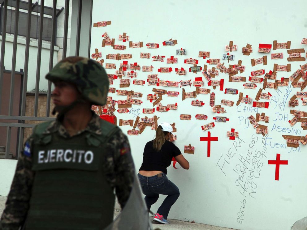 PHOTO: A protester tapes Honduran money inscribed with political slogans alongside crosses representing people killed in post-election violence, on the outside of the central bank in Tegucigalpa, Honduras, Jan. 7, 2018.