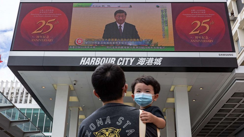 PHOTO: HONG KONG, CHINA: A man holding a child walks in front of a screen showing a live broadcast of Chinese President Xi Jinping speaking during a swearing-in ceremony for Hong Kong's new chief executive John Lee, on July 01, 2022 in Hong Kong, China. 