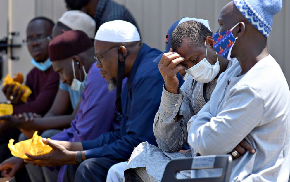 PHOTO: Men from West Africa sit near the site where five people were found dead after a house fire in suburban Denver, Aug. 5, 2020.