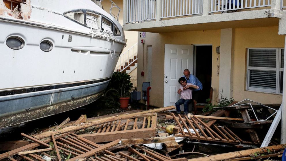 PHOTO: A man helps a woman next to a damaged boat amid a downtown condominium after Hurricane Ian struck in Fort Myers, Florida, Sept. 29, 2022.