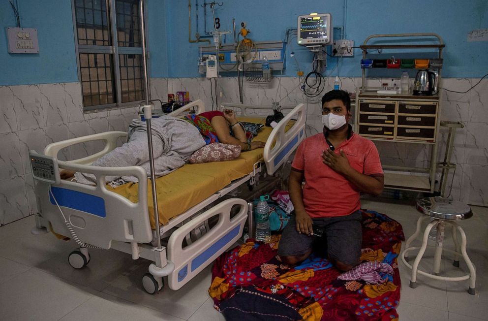PHOTO: A COVID-19 patient lies on a hospital bed as her son sits on the floor beside her, at the Intensive Care Unit (ICU) of Jawahar Lal Nehru Medical College and Hospital,in Bhagalpur, Bihar, India, July 26, 2020. 