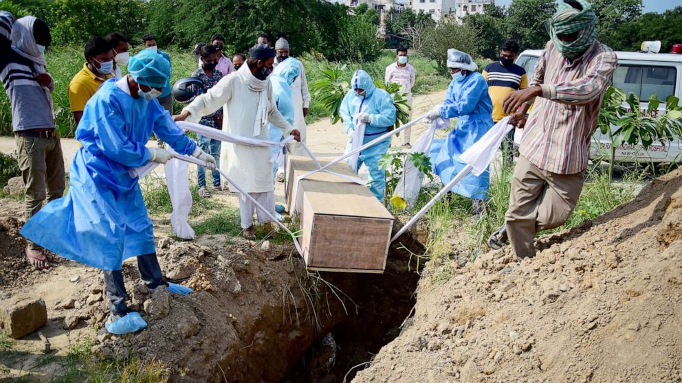 PHOTO: Relatives wearing protective suits as a precaution lower the body of a covid-19 victim for burial at a graveyard in New Nelhi, India, Sept. 3, 2020.
