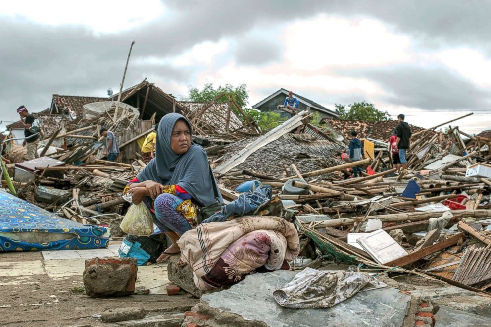 PHOTO: A tsunami survivor sits on a piece of debris as she salvages items from the location of her house in Sumur, Indonesia, Dec. 24, 2018.