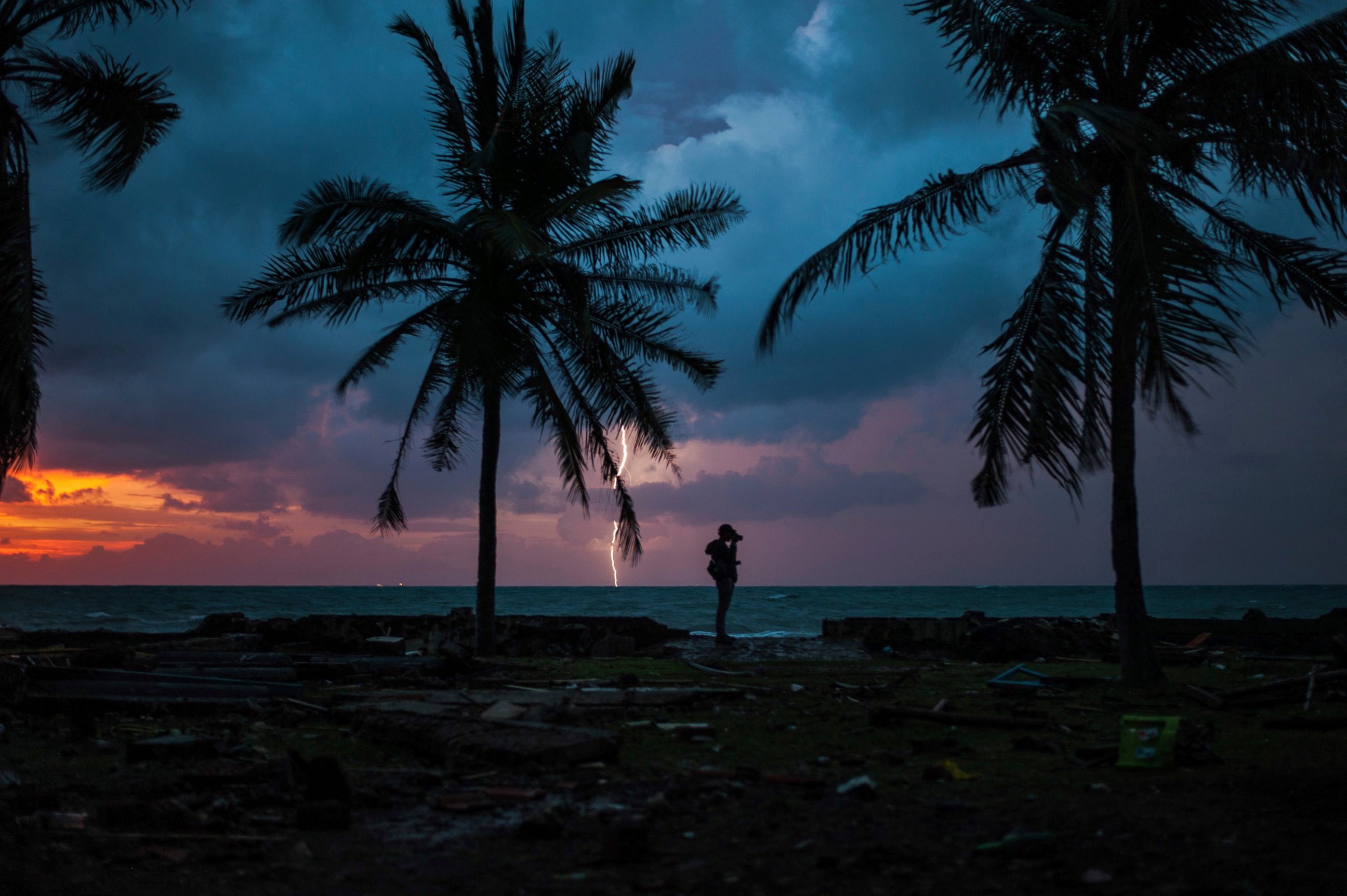 PHOTO: A photojournalist is silhouetted by the sunset as a lightning strike at a resort affected by Saturday's tsunami in Carita, Indonesia, Tuesday, Dec. 25, 2018.