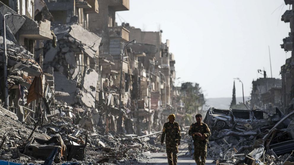 PHOTO: Fighters of the Syrian Democratic Forces (SDF) walk down a street in Raqa past destroyed vehicles and heavily damaged buildings on October 20, 2017, after a Kurdish-led force expelled Islamic State (IS) group fighters from the northern Syrian city.