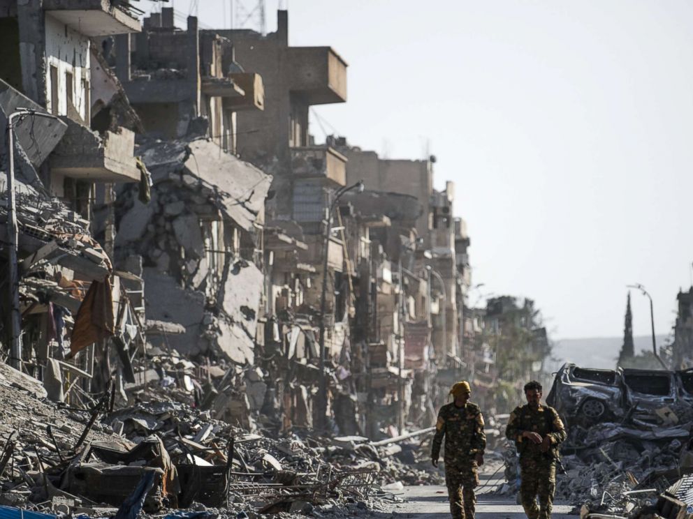 PHOTO: Fighters of the Syrian Democratic Forces (SDF) walk down a street in Raqa past destroyed vehicles and heavily damaged buildings on October 20, 2017, after a Kurdish-led force expelled Islamic State (IS) group fighters from the northern Syrian city.