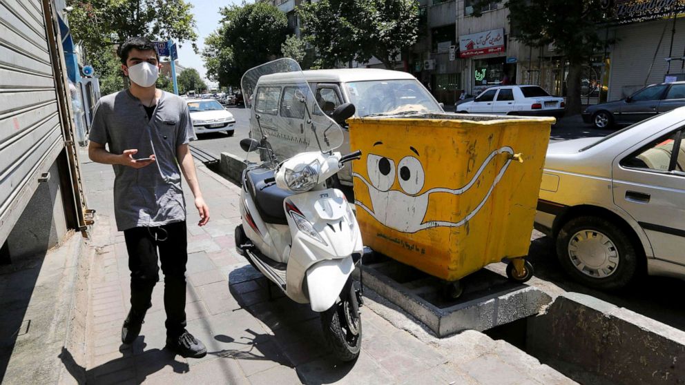PHOTO: An Iranian man walks past a street bin, painted with a drawing of a mask in a campaign to spread awareness over the COVID-19 pandemic, in Tehran, July 18, 2020.
