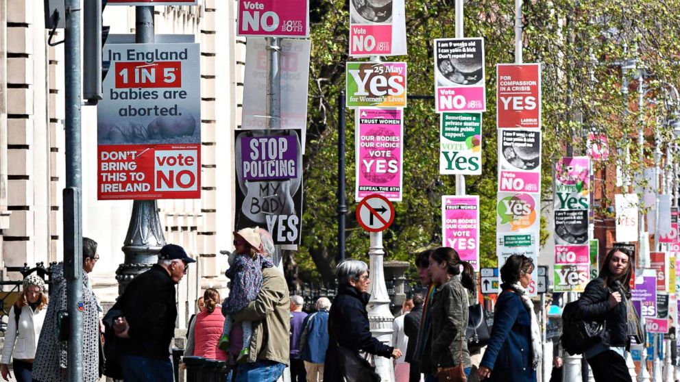 People pass posters urging a yes vote in the referendum to repeal the eighth amendment of the Irish constitution, a subsection that effectively outlaws abortion in most cases, and posters calling for a no vote near the government buildings in Dublin on May 12, 2018.