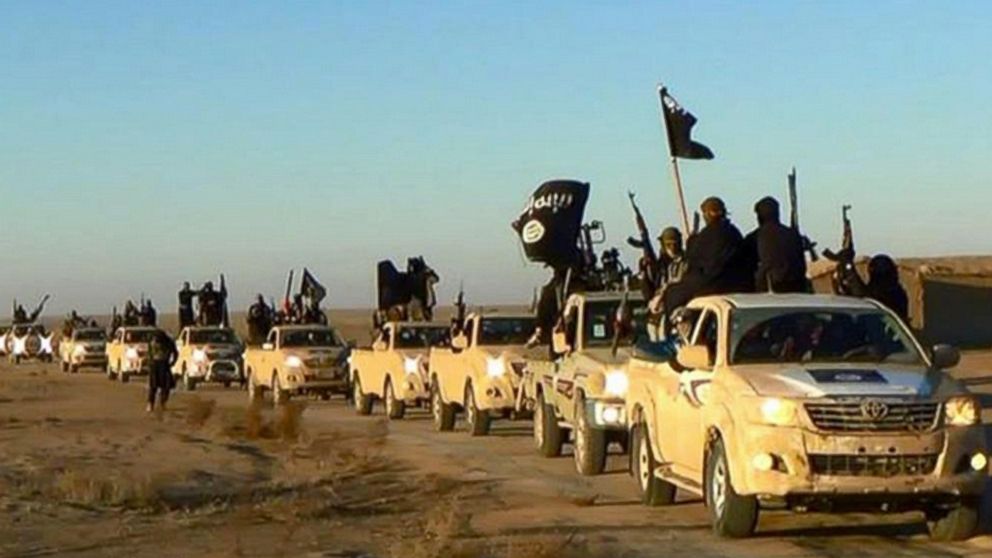 In this undated file photo released online in the summer of 2014, which has been verified and is consistent with other AP reporting, ISIS militants hold up their weapons and wave flags in a convoy on a road leading to Iraq, in Raqqa, Syria.
