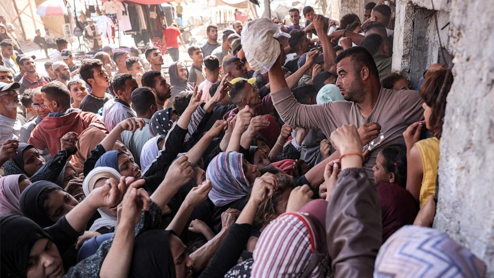 PHOTO: A man prepares to toss a bag of bread for another person as people crowd while queueing for bread outside a bakery in Khan Younis in the southern Gaza Strip, Oct. 23, 2024.