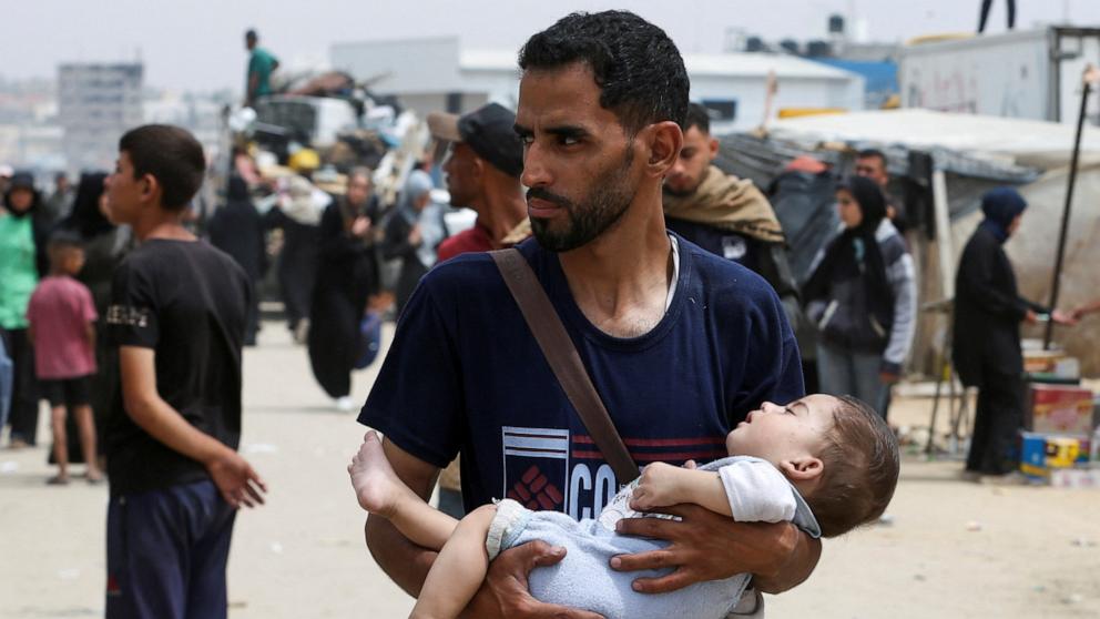 PHOTO: A man carries a child, as Palestinians travel on foot along with their belongings as they flee Rafah due to an Israeli military operation, in Rafah, in the southern Gaza Strip, May 28, 2024. 