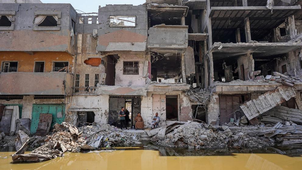 PHOTO: Palestinians sits outside a building destroyed in previous Israeli bombardment, overlooking a pool of stagnant water in Khan Yunis in the southern Gaza Strip, July 19, 2024.