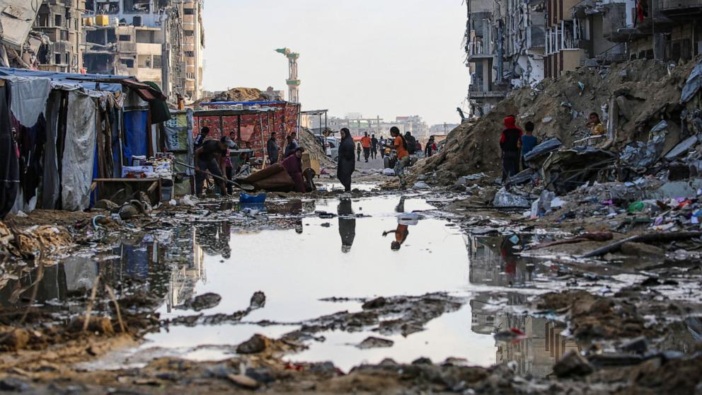 PHOTO: Displaced Palestinians walk around a puddle in front of destroyed buildings and tents in Khan Yunis in the southern Gaza Strip, May 16, 2024.