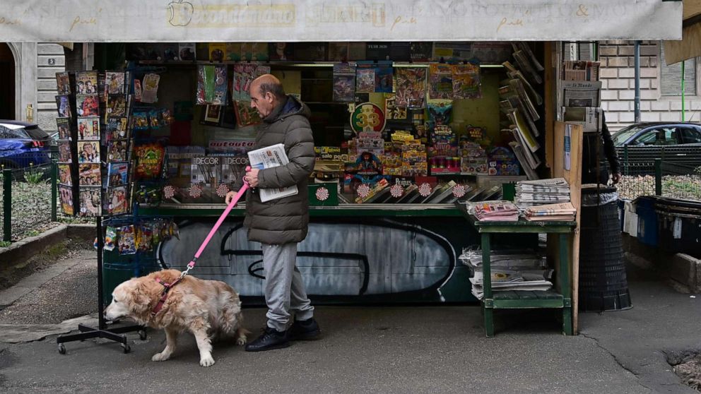 PHOTO: An elderly resident walks his dog and buys a newspaper at a newstand in Milan, March 12, 2020.