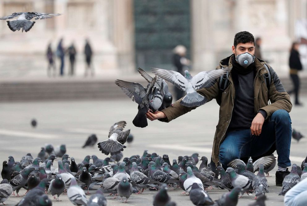 A man in a face mask feeds pigeons in Milan, Italy, as the country is hit by the novel coronavirus outbreak, Feb. 25, 2020.Yara Nardi/Reuters