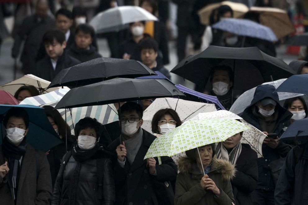 PHOTO: Pedestrians holding umbrellas wear face masks as they walk on a road in Tokyo, Japan, on Feb. 13, 2020.