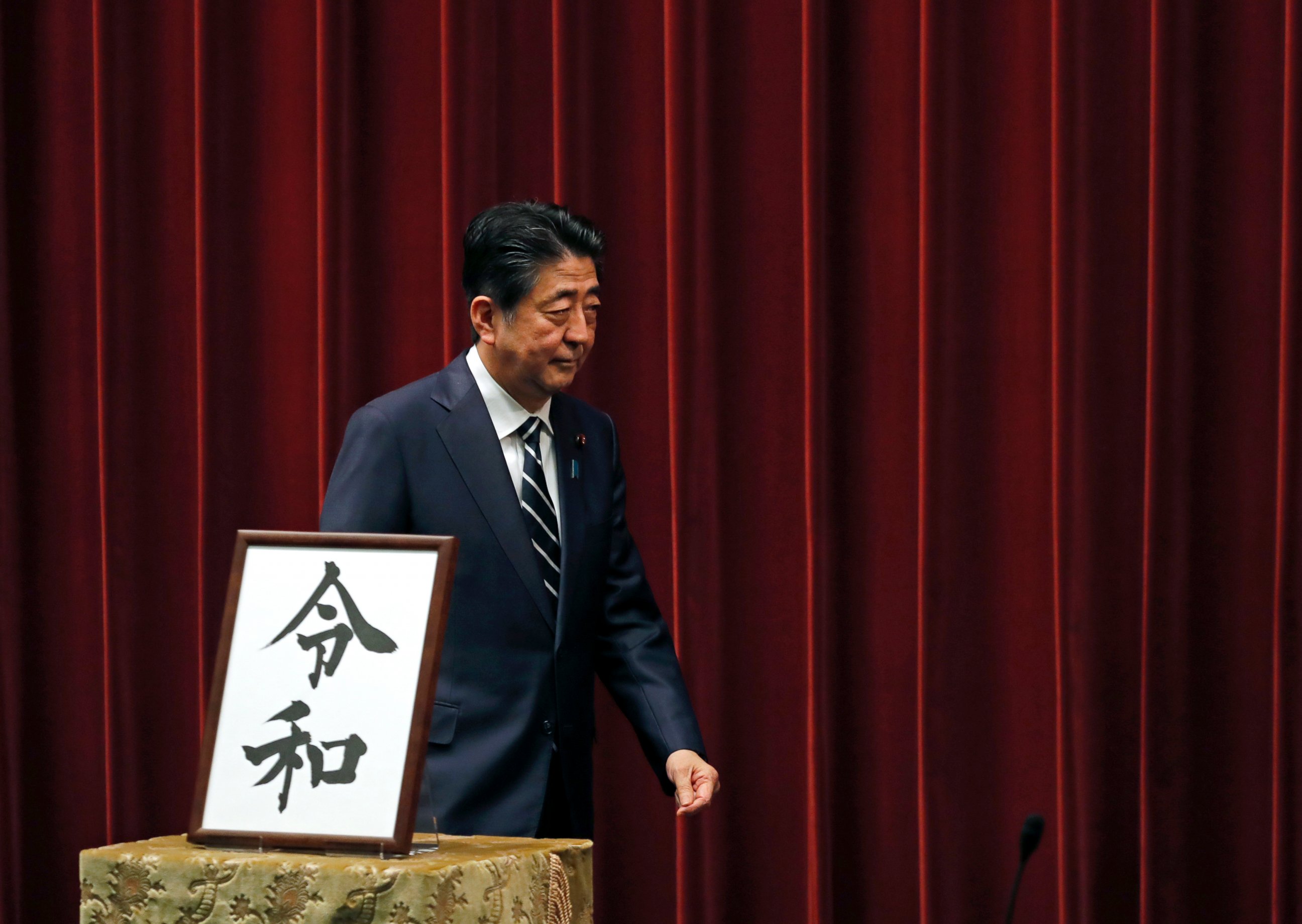 PHOTO: Japanese Prime Minister Shinzo Abe walks past the name of new era "Reiwa" on display at the Prime Minister's office in Tokyo, Monday, April 1, 2019.