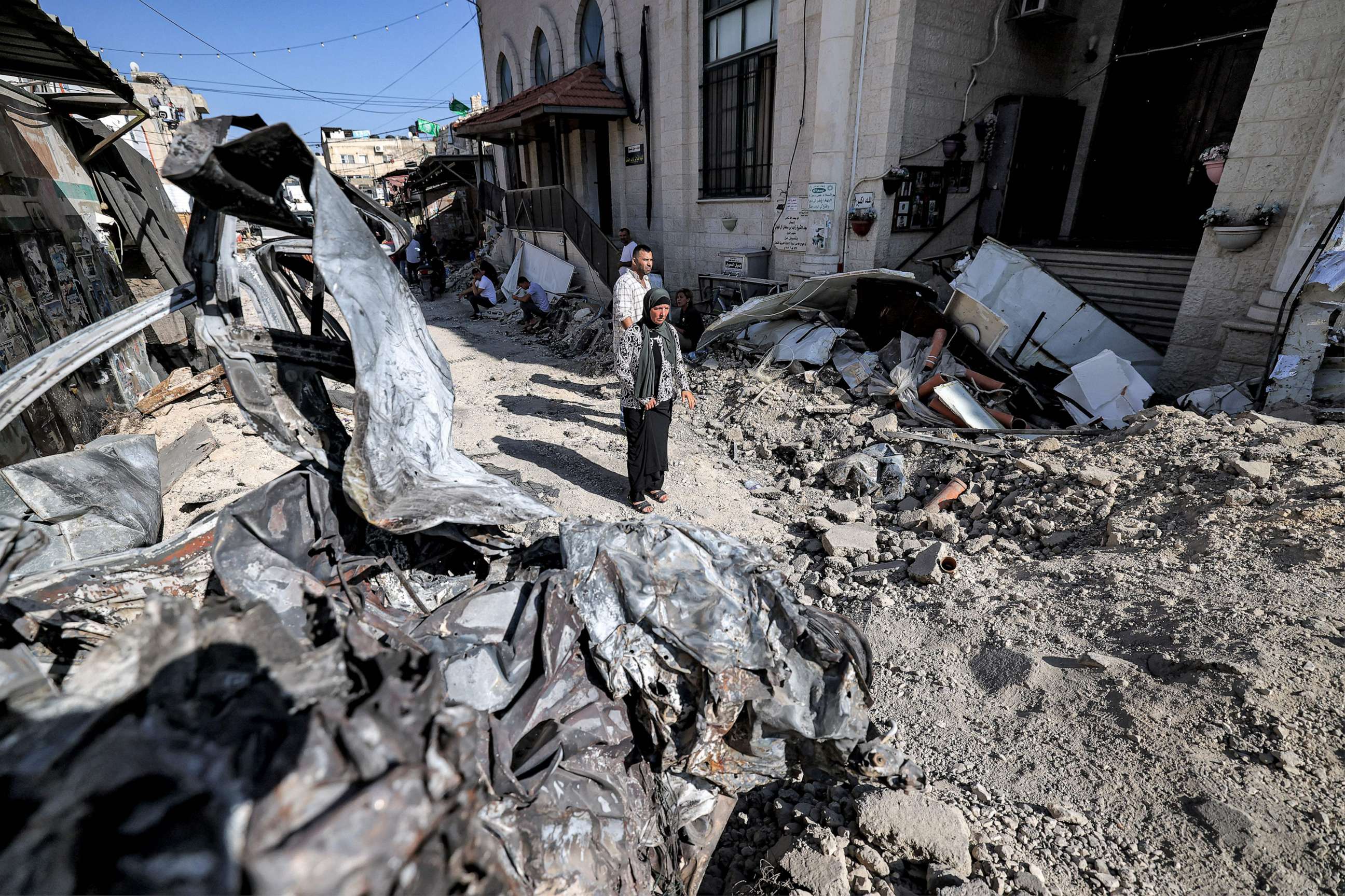 PHOTO: People stand by rubble and the remains of a destroyed vehicle outside a mosque in the occupied West Bank city of Jenin, July 5, 2023, after the Israeli army declared the end of a two-day military operation in the area.