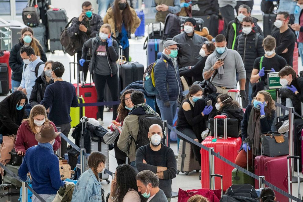 PHOTO: Passengers wear face masks to fend off coronavirus as they wait in line to check in for their flights, March 24, 2020, at JFK airport in New York.