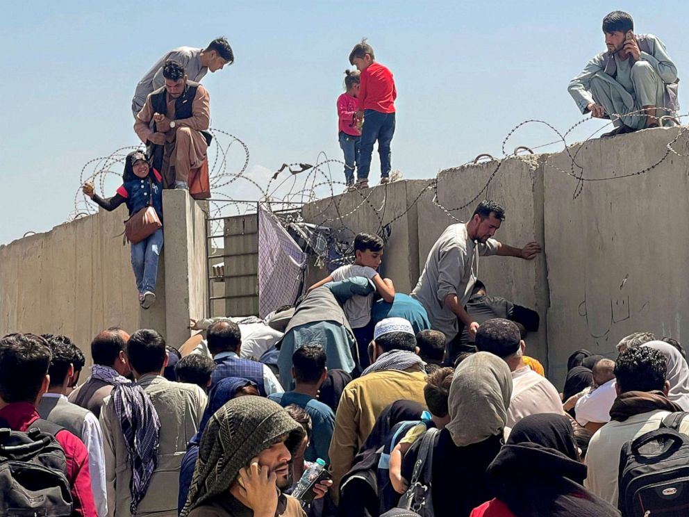 PHOTO: A man, left, helps a young girl over the concrete barrier into Hamid Karzai International Airport in Kabul, Aug. 16, 2021.
