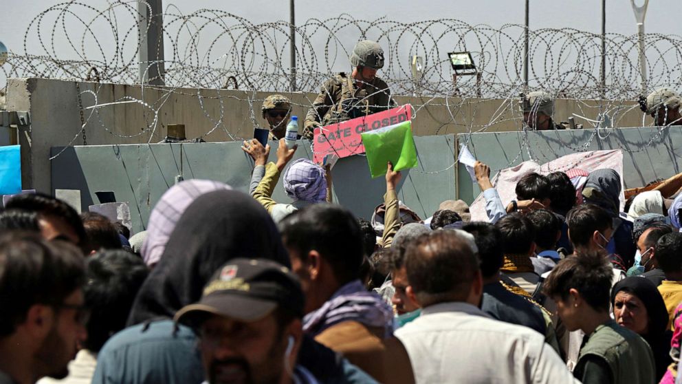PHOTO: A U.S. soldier holds a sign indicating a gate is closed as hundreds of people gather, some holding documents, near an evacuation control checkpoint on the perimeter of the Hamid Karzai International Airport, in Kabul,  Aug. 26, 2021.