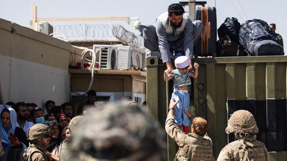 PHOTO: An Afghan man hands his child to a British Paratrooper assigned to 2nd Battalion, Parachute Regiment while a member of 1st Brigade Combat Team, 82nd Airborne Division conducts security at Hamid Karzai International Airport in Kabul, Aug. 26, 2021.