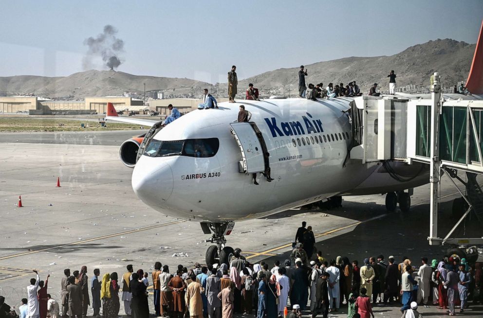 PHOTO: Afghan people climb atop a plane as they wait at the Kabul airport in Kabul, Afghanistan, Aug. 16, 2021.