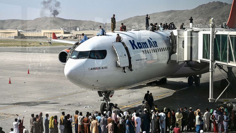 PHOTO: Afghan people climb atop a plane as they wait at the Kabul airport in Kabul, Aug. 16, 2021.
